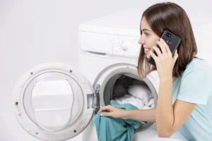 Woman talking on a phone while loading laundry into an open washing machine doo